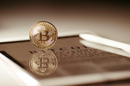Gold Bitcoin coin reflected on a tablet showing the Bitcoin whitepaper