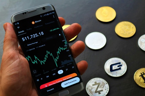 Hand holding a phone with a Bitcoin wallet app next to cryptocurrency coins