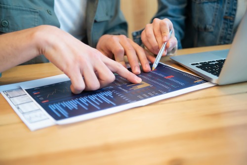 Two people reviewing financial charts on paper and a laptop